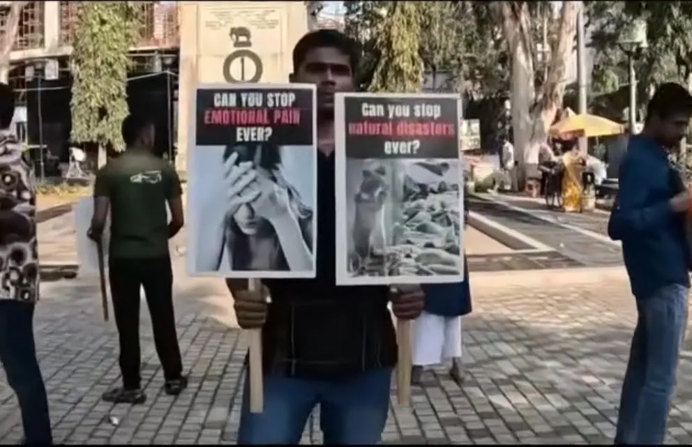 Protest in India: an activist holds two signs asking "Can you stop emotional pain ever?" and "Can you stop natural disasters ever?"